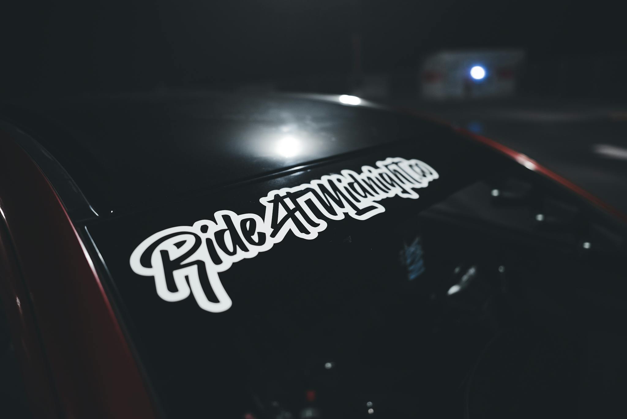 A close-up of a car windshield with a 'Ride at Midnight' sticker in a dark setting.
