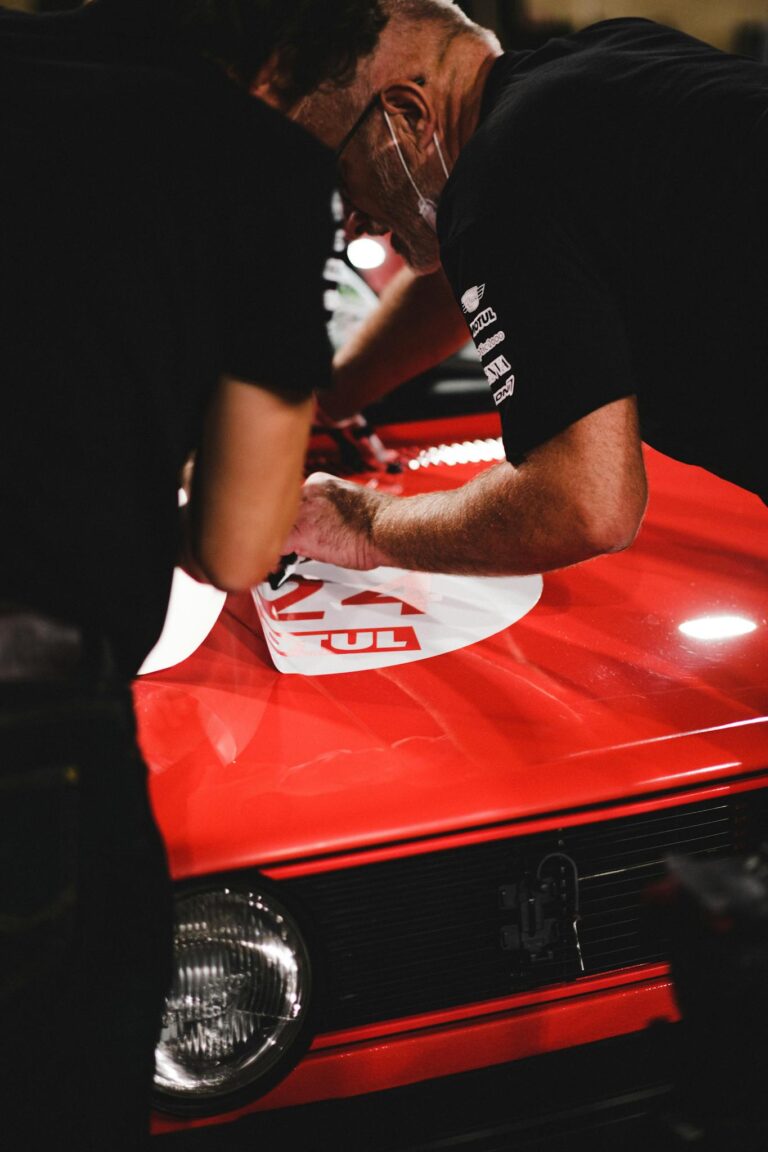 Men work on a red car applying decals, highlighting teamwork and precision.